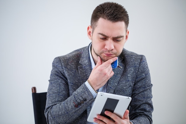 Succesvolle zakenman zakenman in een pak zittend op een houten stoel met een tablet en kijken naar het scherm. Op een witte achtergrond met gedachten aan een nieuw project