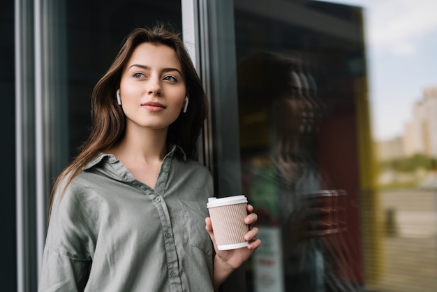 Succesvolle zakenvrouw luisteren naar muziek, houden kopje koffie lopend op straat