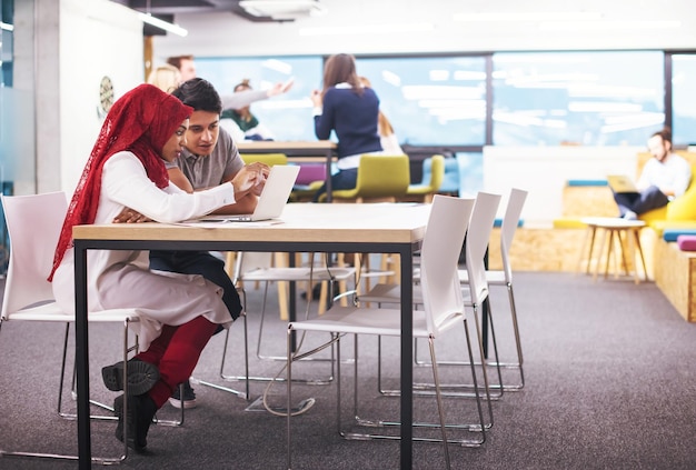 succesvolle zwarte moslim zakenvrouw die een ontmoeting heeft met haar Indiase mannelijke collega die op de laptop werkt op een modern startkantoor