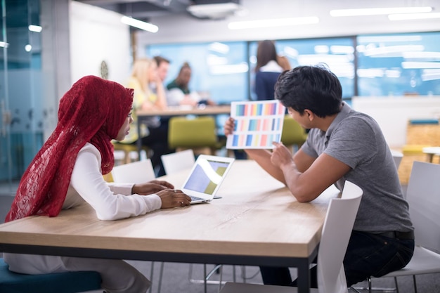 succesvolle zwarte moslim zakenvrouw die een ontmoeting heeft met haar Indiase mannelijke collega die op de laptop werkt op een modern startkantoor