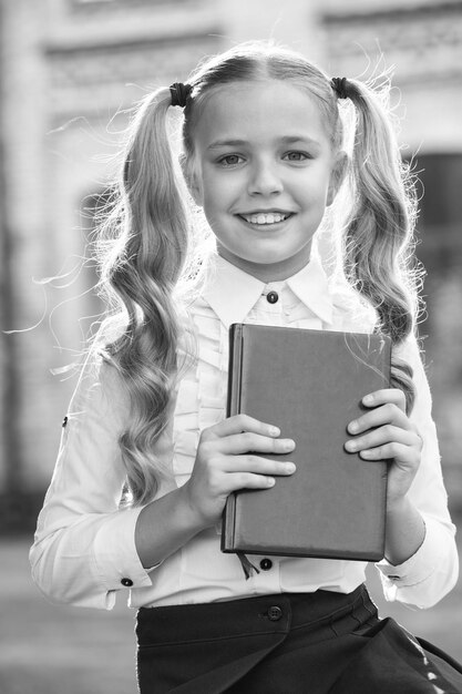 Фото Такая интересная книга счастливый ребенок держит книгу на открытом воздухе снова в школу взгляд девочки формальная форма школьная мода детское образование день защиты детей