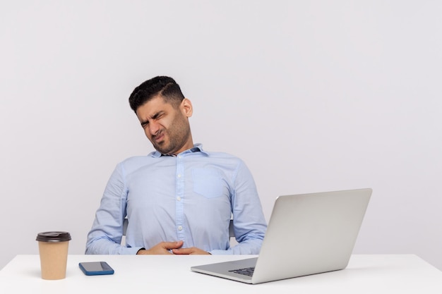 Sudden stomach ache at work Unhealthy man employee sitting in office suffering heartburn gastrointestinal disorder symptoms of constipation indigestion studio shot isolated on white background