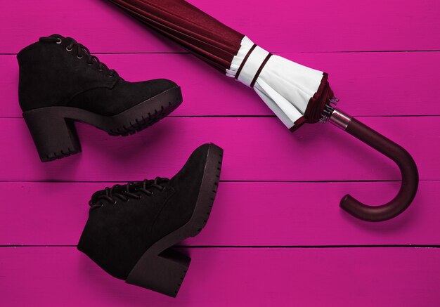 Suede black boots, umbrella on pink wooden background. Top view