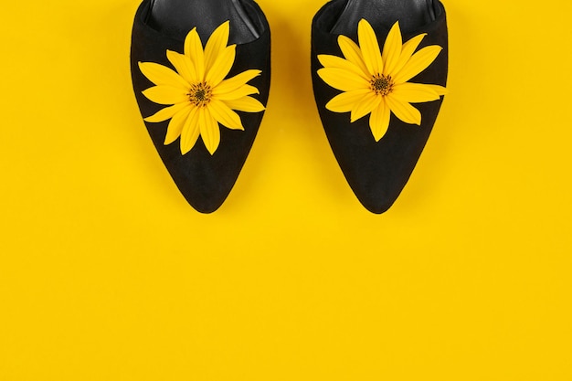 Suede black court shoes with yellow Topinambur flower bud on yellow background womanhood concept