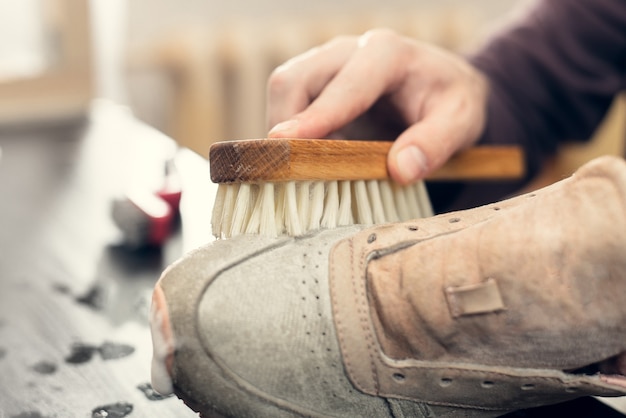 Suède sneakers schoonmaken. Een arbeider in een schoenenatelier maakt een stapel schoenen schoon.