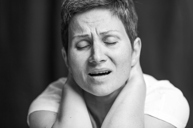 Suffering emotion on the face of an adult woman with a short gray hair. Black and white portrait.