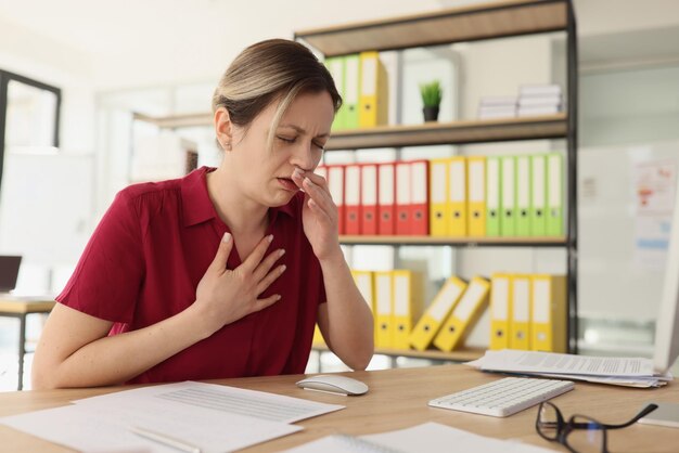 Suffering female employee coughs sitting at office workplace