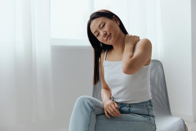 Suffering from shoulder dislocation neuralgia tanned beautiful\
young asian woman touching painful shoulder at home interior living\
room injuries poor health illness concept cool offer banner