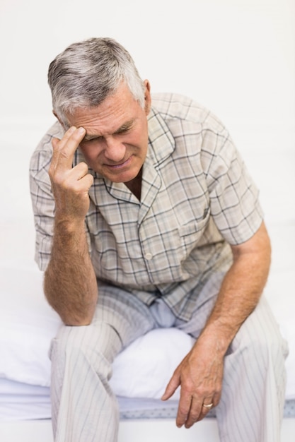 Uomo senior di sofferenza che tocca la sua fronte a casa