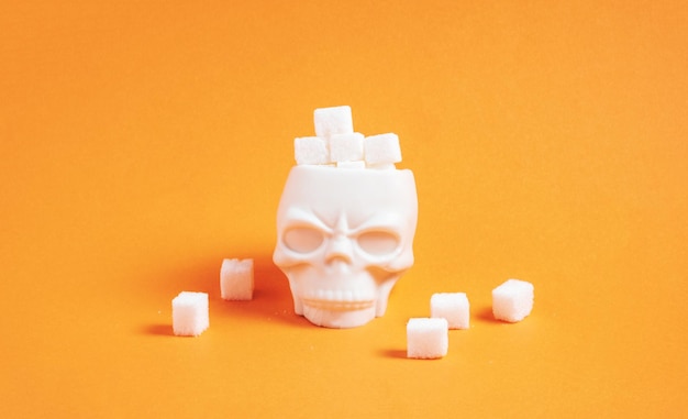 Sugar cubes in container in shape of skull on orange background