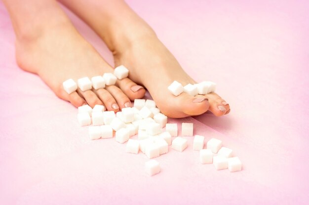 コピースペース、脱毛の概念とピンクの背景に女性の足に並んで横たわっている砂糖の立方体。
