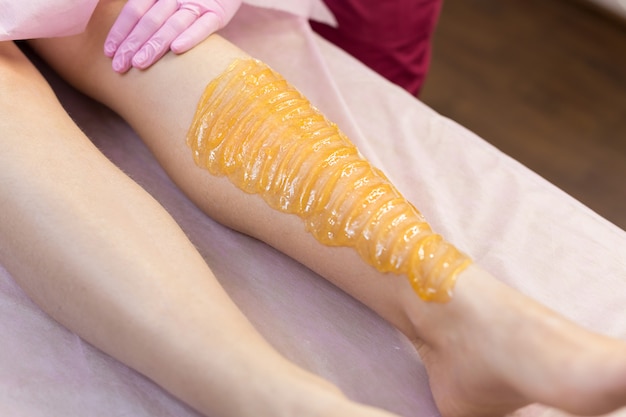 Photo sugar depilation of the feet in the beauty salon. rid of hair on the legs. sugaring. master shugaring applies thick sugar paste on the legs of a young girl, removing hair on the legs. close-up.