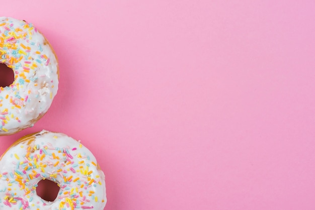 Foto ciambelle di zucchero con glassa di cioccolato e spruzza su sfondo rosa