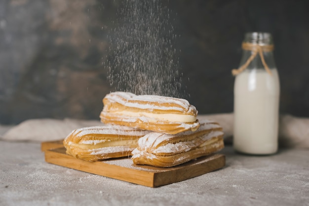 Sugar dusting on eclair over the wooden chopping board