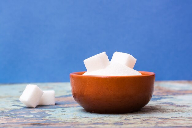 Sugar granulated and refined sugar in a bowl on a wooden table on a blue background