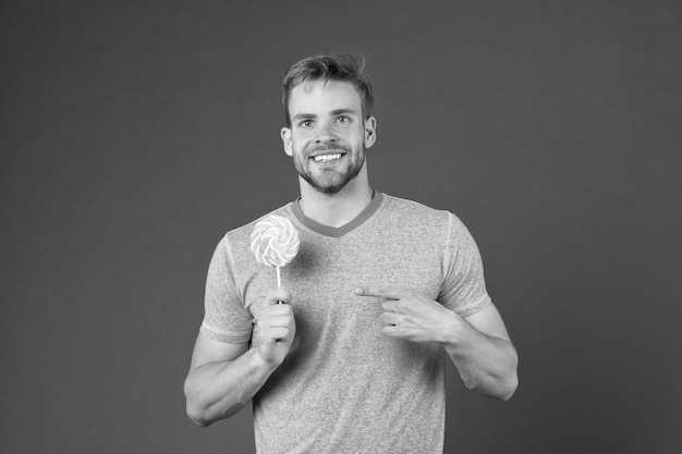 Sugar harmful for health Guy hold lollipop candy violet background Man handsome macho eat big colorful sweet lollipop Taste of childhood Man bearded adult likes lollipop Sweet tooth concept