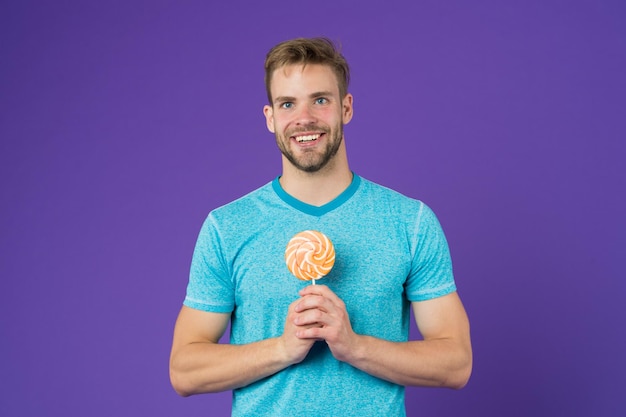 Sugar harmful for health Guy hold lollipop candy violet background Man handsome macho eat big colorful sweet lollipop Taste of childhood Man with bristle likes lollipop Cheat meal concept