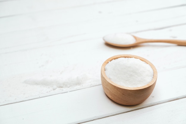 Sugar is in a wooden bowl placed on a white table.