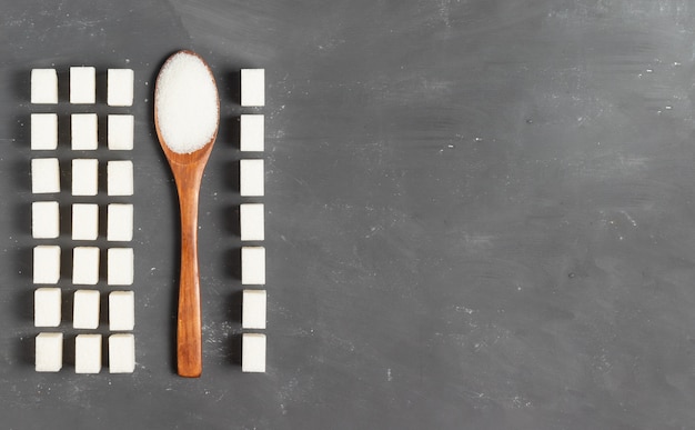 Sugar lumps with a wooden eco spoon filled with loose sugar on a gray background