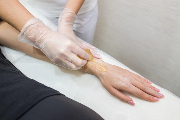 Sugar paste hair removal procedure shugaring cosmetologist\
applies sugar paste to the hand of a young womandepilation of\
female hands in a beauty parlor