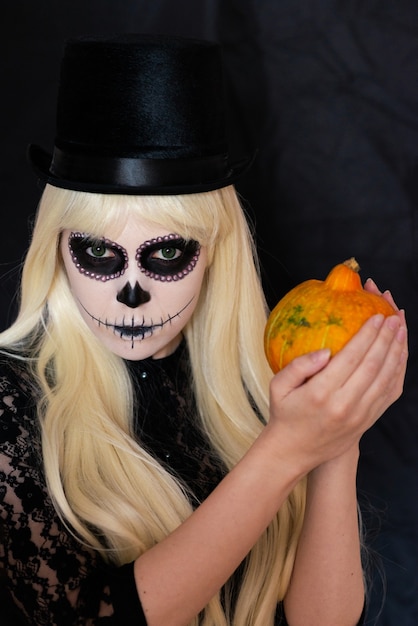 Sugar skull girl with blond in black hat, studio shot. Copy space.