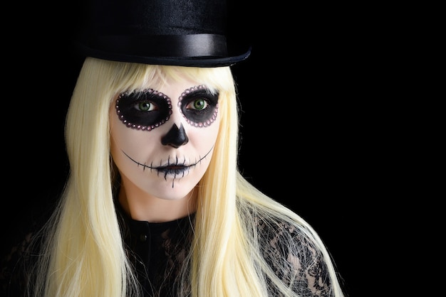 Sugar skull girl with blond in black hat, studio shot. Copy space.