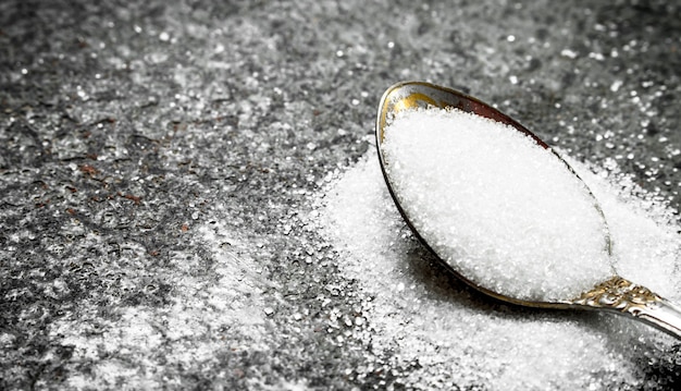 Sugar in a teaspoon. On a rustic background.