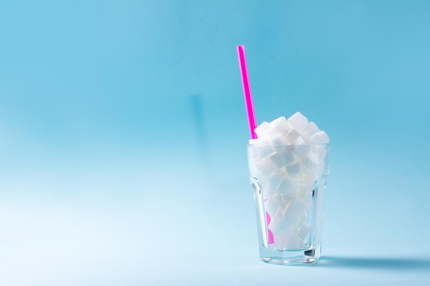 写真 ガラスの砂糖の白い立方体糖尿病と砂糖の使いすぎの概念青い背景にコピー スペース