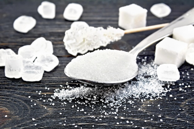 Sugar white granulated in a metal spoon, crystal and cubes on a wooden plank background