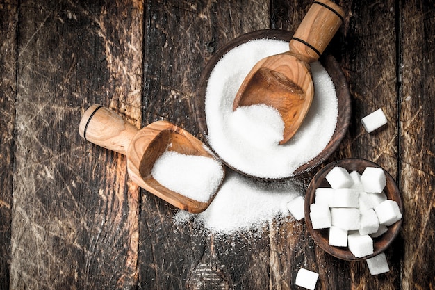 Sugar with a scoop in a bowl. On a wooden background.