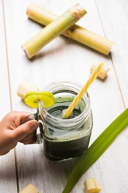 Sugarcane Juice OR Ganne Ka Ras in a glass or Jar with cut pieces of cane over colourful or wooden background. selective focus