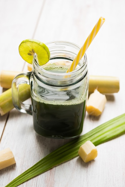 Photo sugarcane juice or ganne ka ras in a glass or jar with cut pieces of cane over colourful or wooden background. selective focus