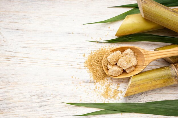 Sugarcane with green leaf and pieces of brown sugar in a wooden spoon on a beige background space for text Top view