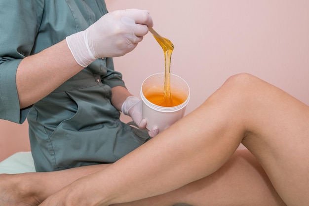 Sugaring process in a beauty salonCosmetologist woman applying wax or sugar on young girls leg before the epilation or depilation procedure