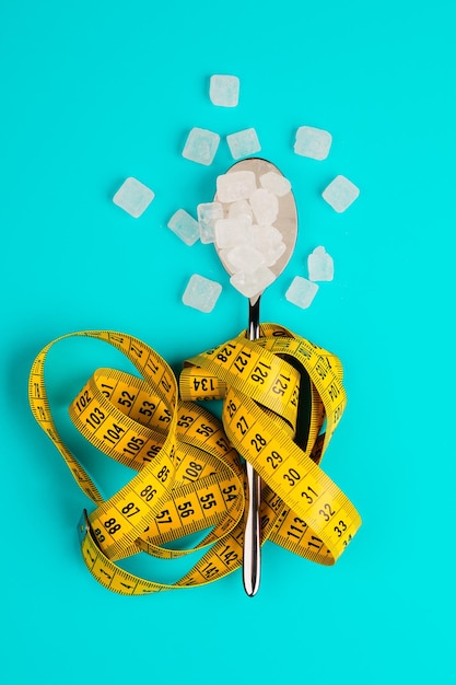 Sugarreplacing tablets or sugar with a spoon are entangled in the measuring tape On a blue background The concept of diabetes and proper nutrition