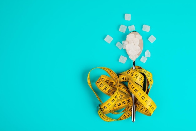 Sugarreplacing tablets or sugar with a spoon are entangled in the measuring tape On a blue background The concept of diabetes and proper nutrition