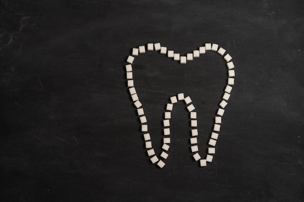 Suiker vernietigen tandglazuur leidt tandbederf witte suikerklontjes vorm tand bruin suiker cariës zwarte achtergrond gezondheidszorg en geneeskunde stomatologie concept zoet voedsel tanden vernietigen