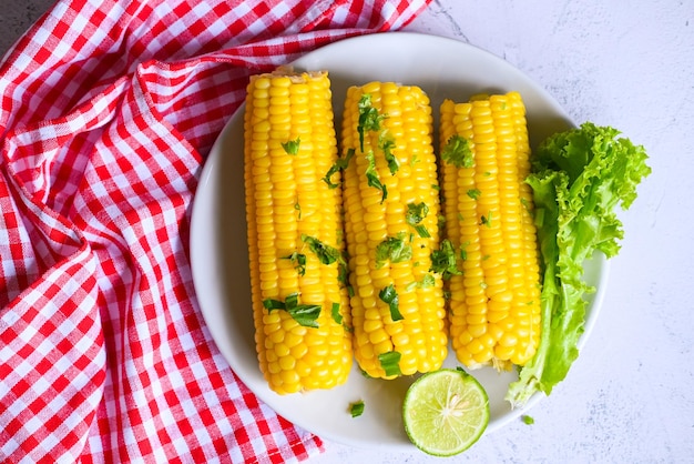 Suikermaïs eten met salade plantaardige limoen koriander en sla rijpe maïskolven gestoomde of gekookte suikermaïs voor voedsel veganistisch diner of snack zoete maïs gekookt op witte plaat achtergrond