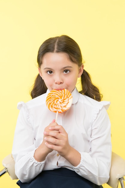 Suikerverslaving Meisje schattige jongen paardenstaarten kapsel eet zoete lolly Snoepjes in gepaste porties oké Meisje leerling schooluniform houdt van snoep lolly snoep gele achtergrond Haar favoriete smaak