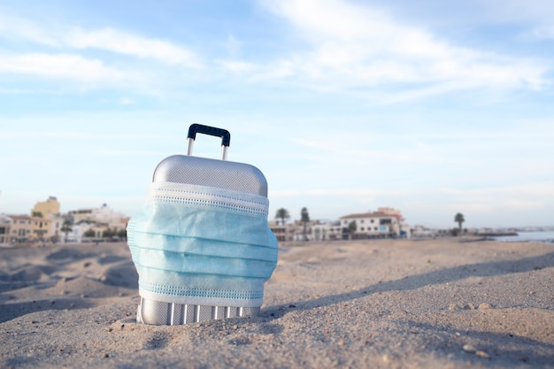 Suitcase for travel with a medical mask on the beach