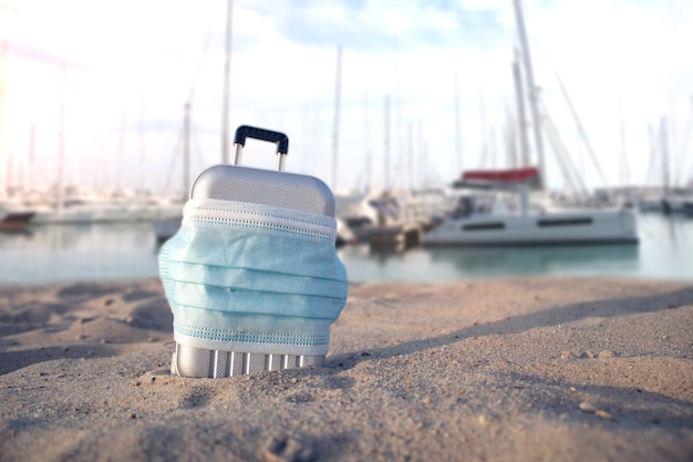 Suitcase for travel with a medical mask on the beach