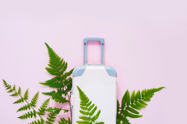 Suitcase and tropical leaves on pink