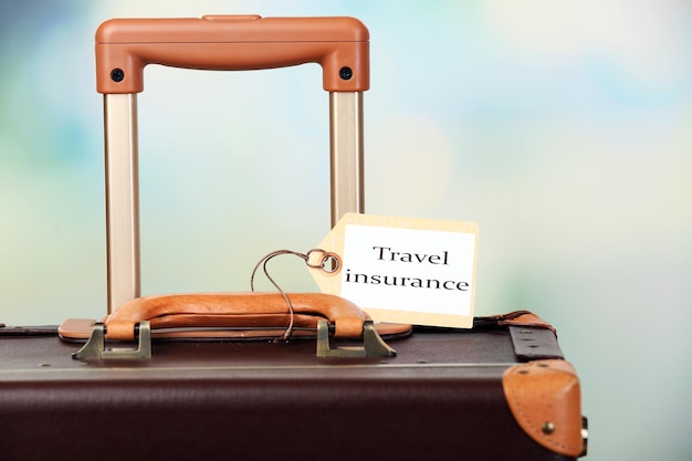 Suitcase with TRAVEL INSURANCE label on light blurred background