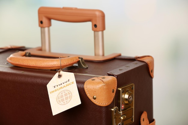 Photo suitcase with travel insurance label on light blurred background