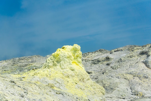 Sulfur deposits around a solfatara in a fumarole field against a blue sky