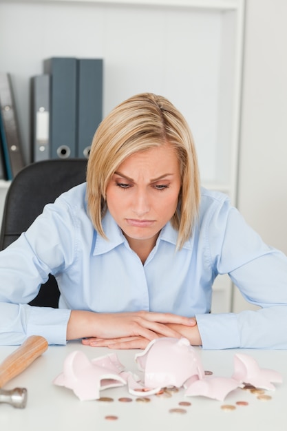 Sulking woman sitting in front of an shattered piggy bank