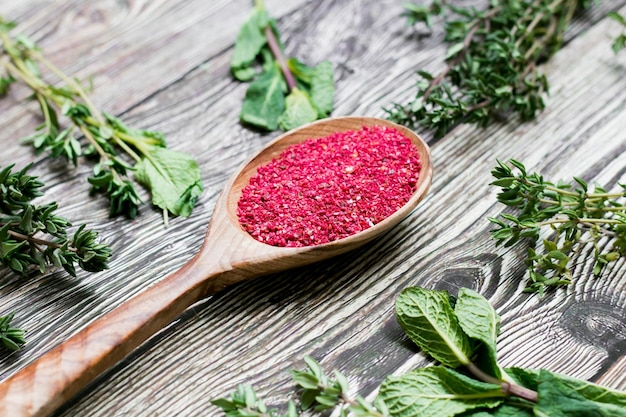 Sumac seeds in a wooden spoon on rustic background red seasoning