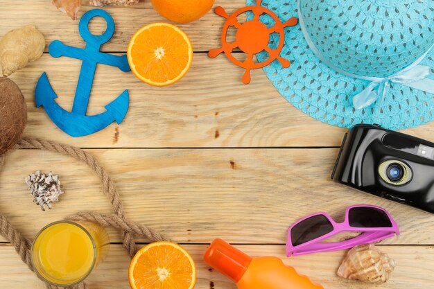 Summer accessories. beach accessories. hat, sunscreen, sunglasses, camera, and orange on a natural wooden table. top view.