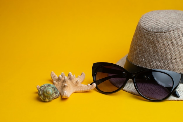 Summer accessories, shells, hat and sunglasses on yellow surface. 