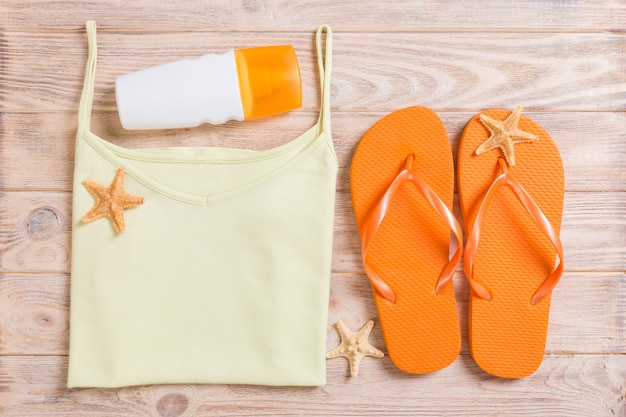 Summer accessories with t-shirt, seashells and straw hat on wooden background top view flat lay.